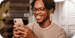 Jovem com óculos e cabelo em tranças curtas sorri enquanto usa smartphone, ilustrando engajamento em campanhas de mídia paga